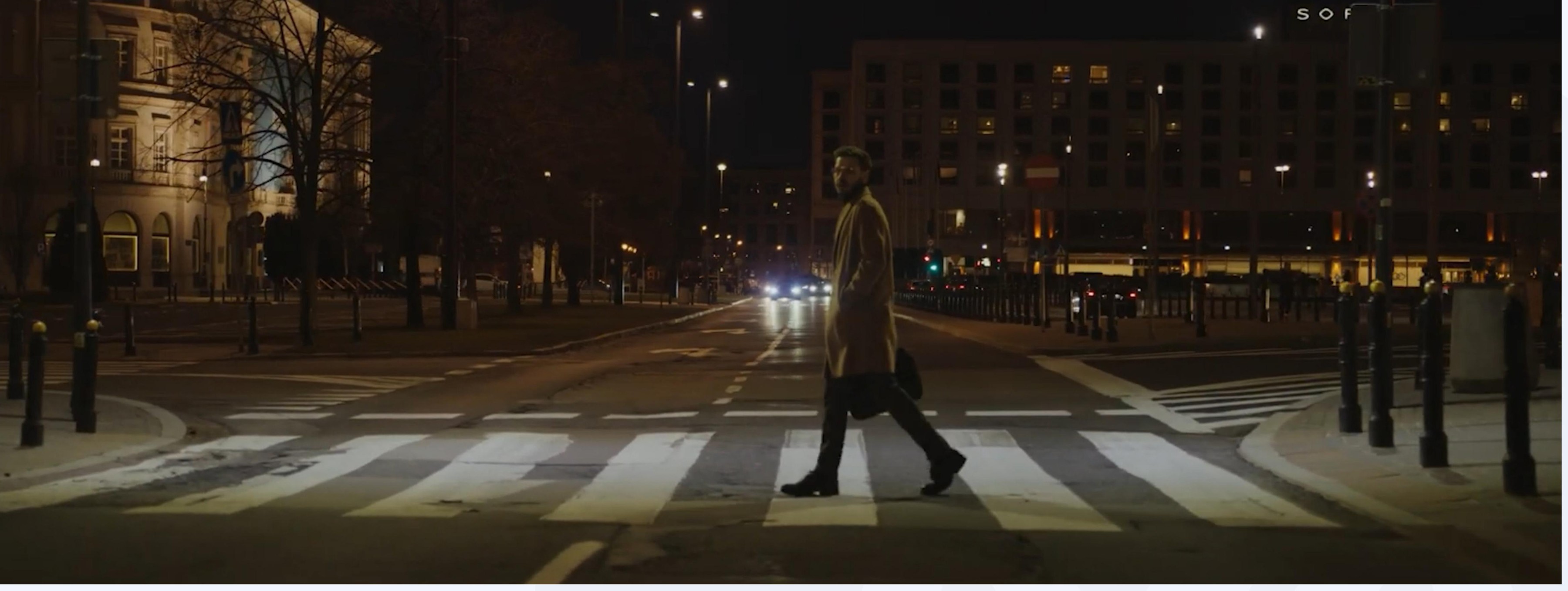 A man crossing a quiet, lamplit street at night