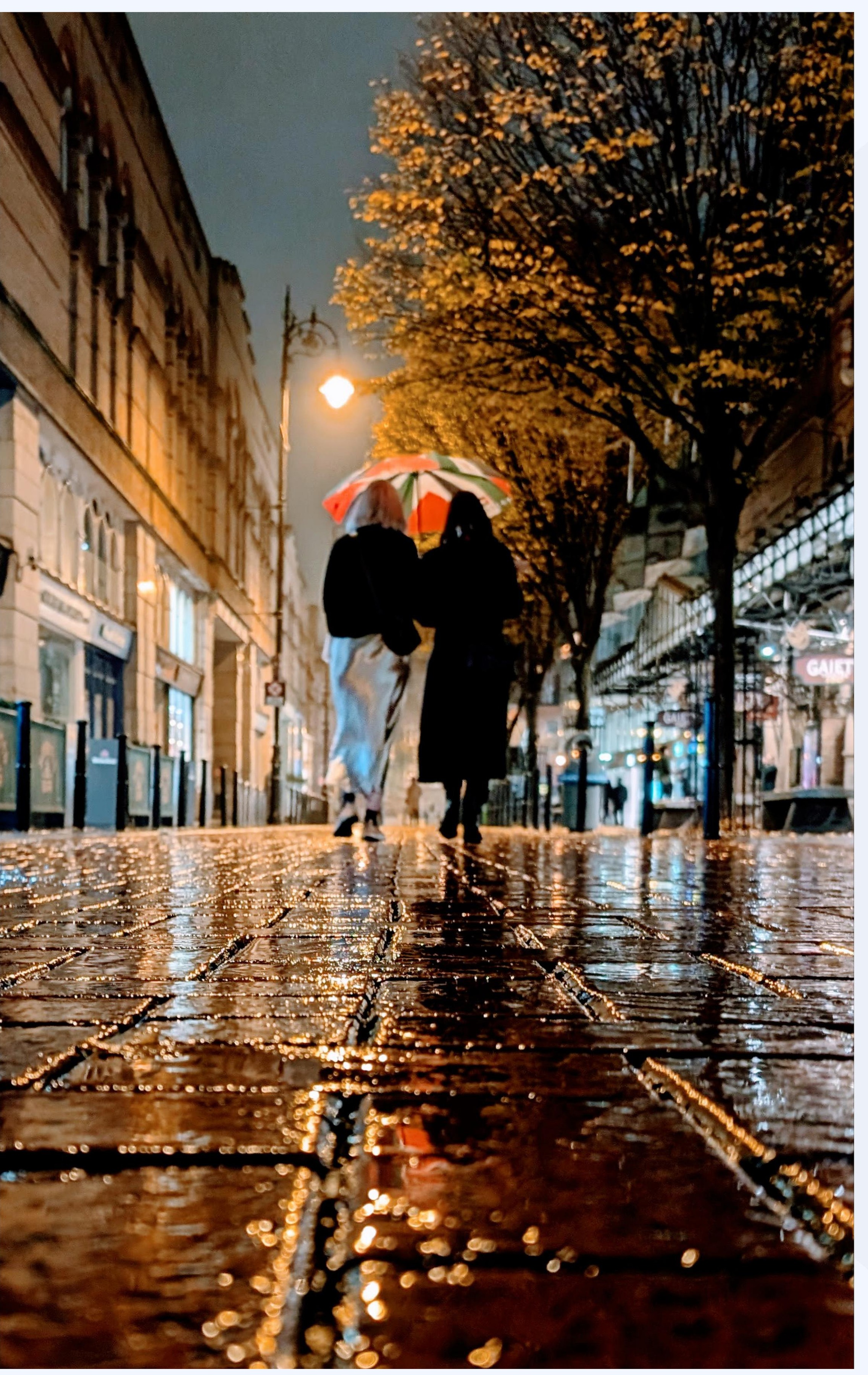 Two people under an umbrella on a rain-soaked street at night