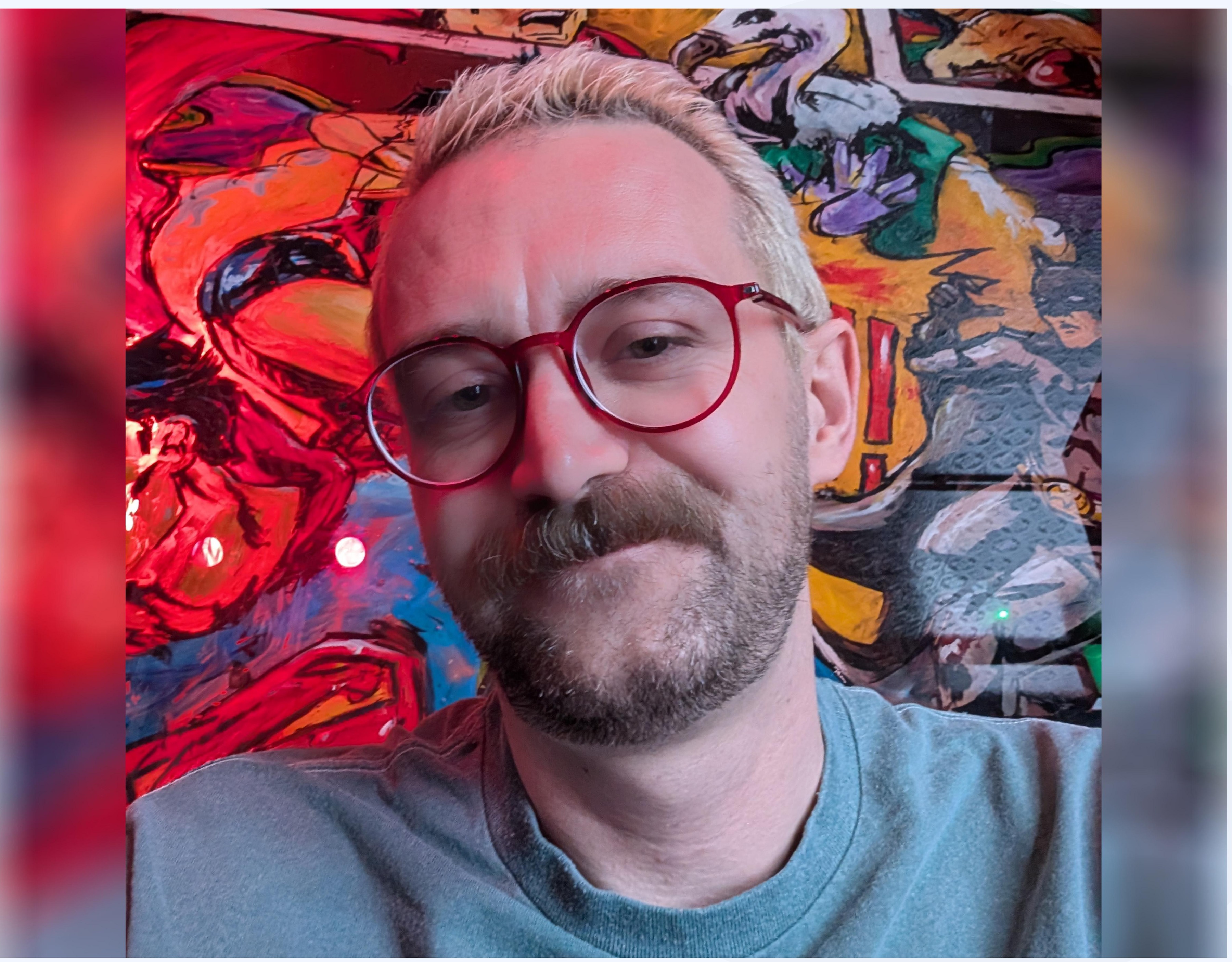 Zach Moroney, portrait, lit by a colourful painting in the background